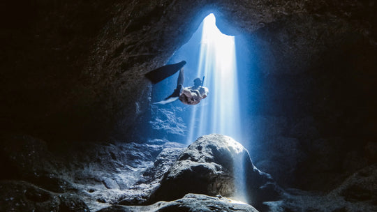 Person exploring a dark cave with a beam of light shining through