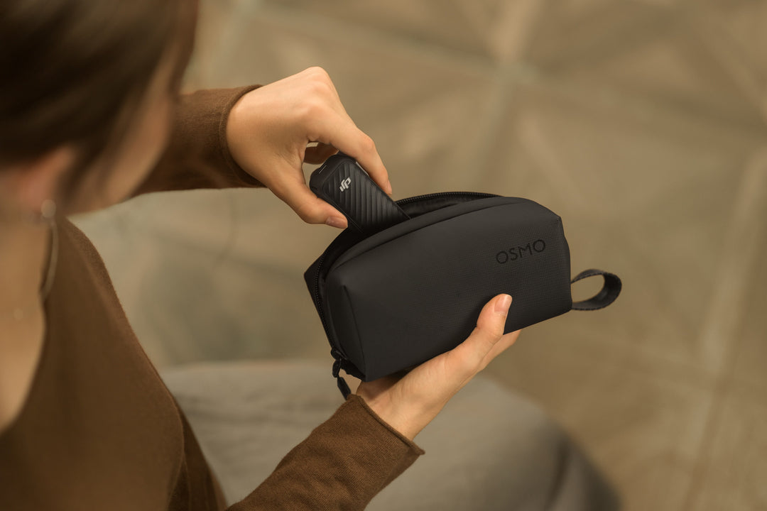 Person holding a black carrying case with 'OSMO' branding against a neutral background