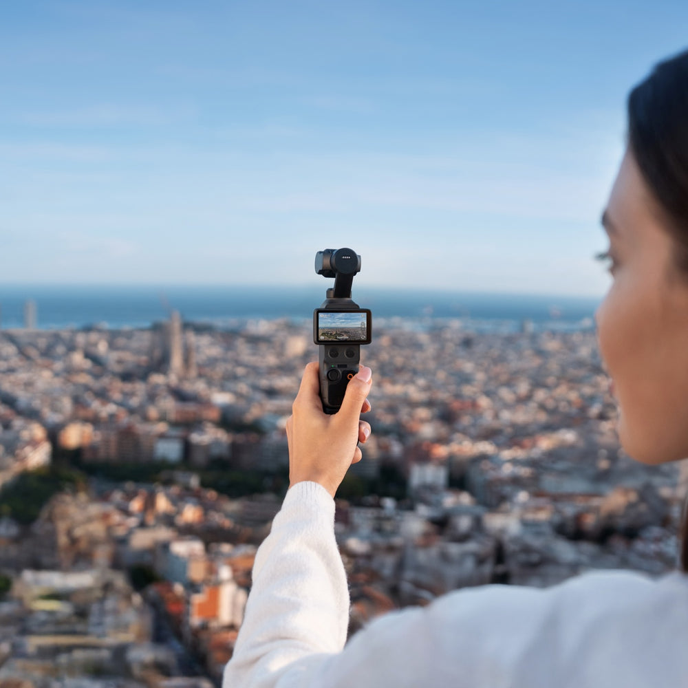 Person holding a dji osmo pocket 4 over a cityscape with a clear blue sky
