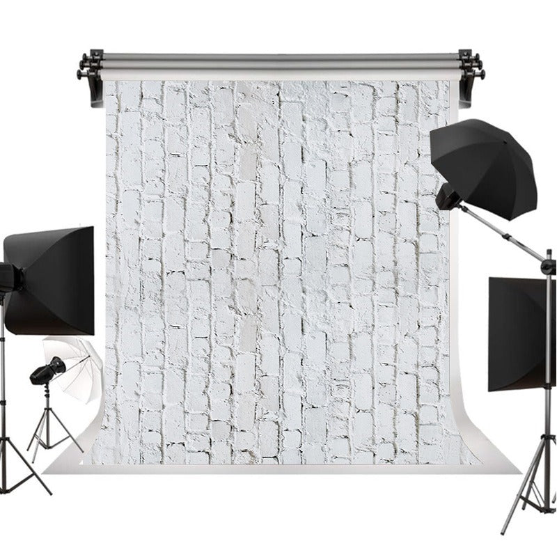 A photography backdrop with a white brick wall pattern, displayed on a stand with studio lighting equipment including softboxes and umbrellas on a white background.