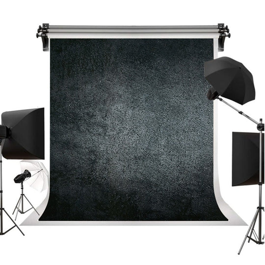 A textured black photography backdrop roll displayed on a white studio background, surrounded by studio lighting equipment including softboxes and a reflector.