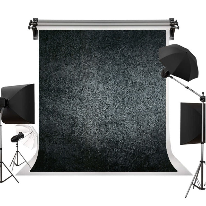 A textured black photography backdrop roll displayed on a white studio background, surrounded by studio lighting equipment including softboxes and a reflector.