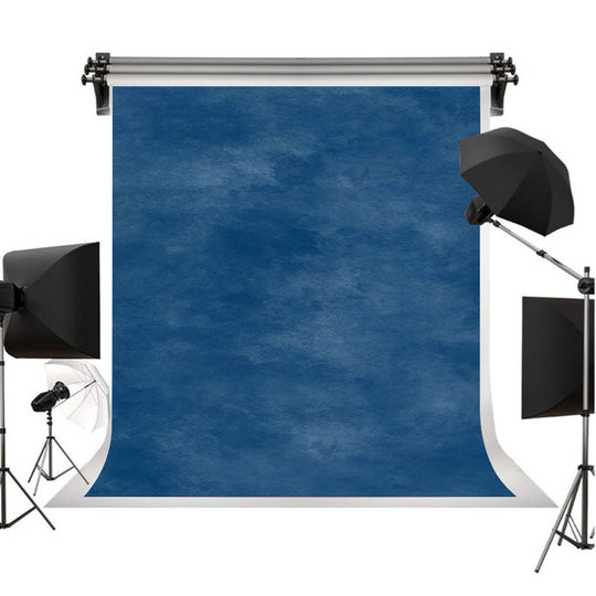A blue textured photography backdrop roll displayed on a stand, surrounded by studio lighting equipment including softboxes and an umbrella on a white background.
