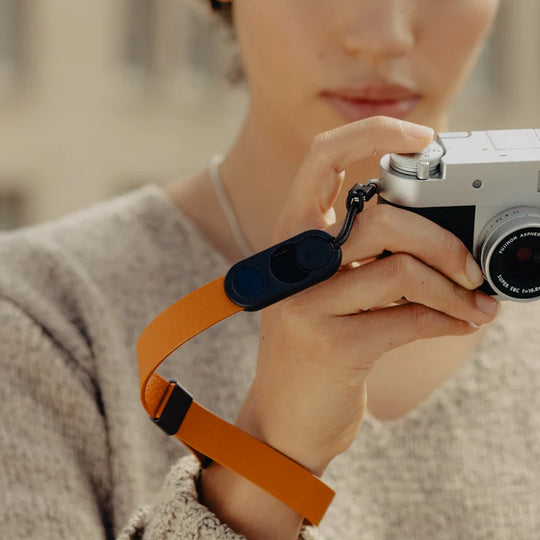 Person holding a camera with an orange strap against a blurred background