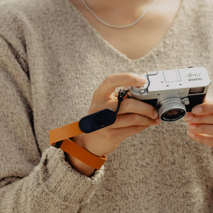 Person holding a vintage camera with an orange strap against a neutral background