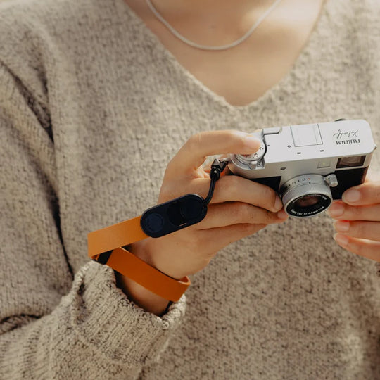 Person holding a vintage camera with an orange strap against a neutral background