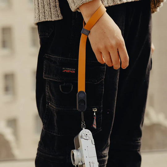 Person holding a camera with an orange strap against a blurred background