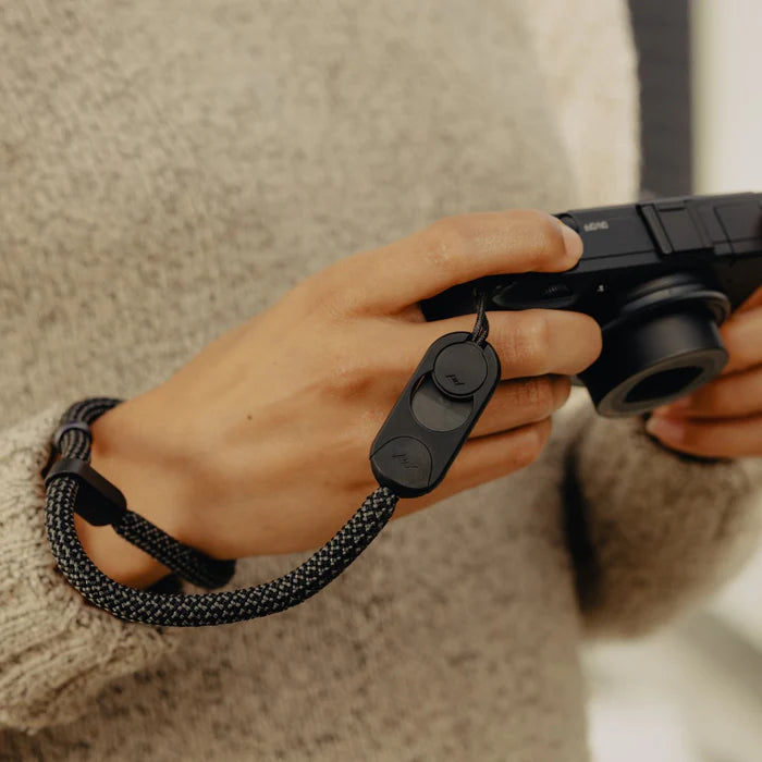 Person holding a camera with a black Peak Design Cuff Rope on a blurred background