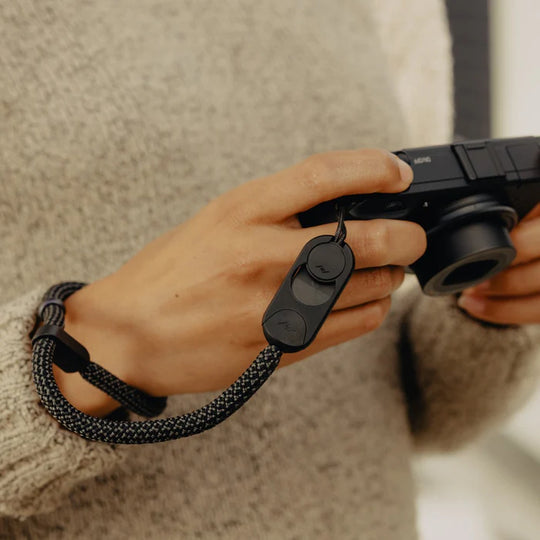 Person holding a camera with a black Peak Design Cuff Rope on a blurred background