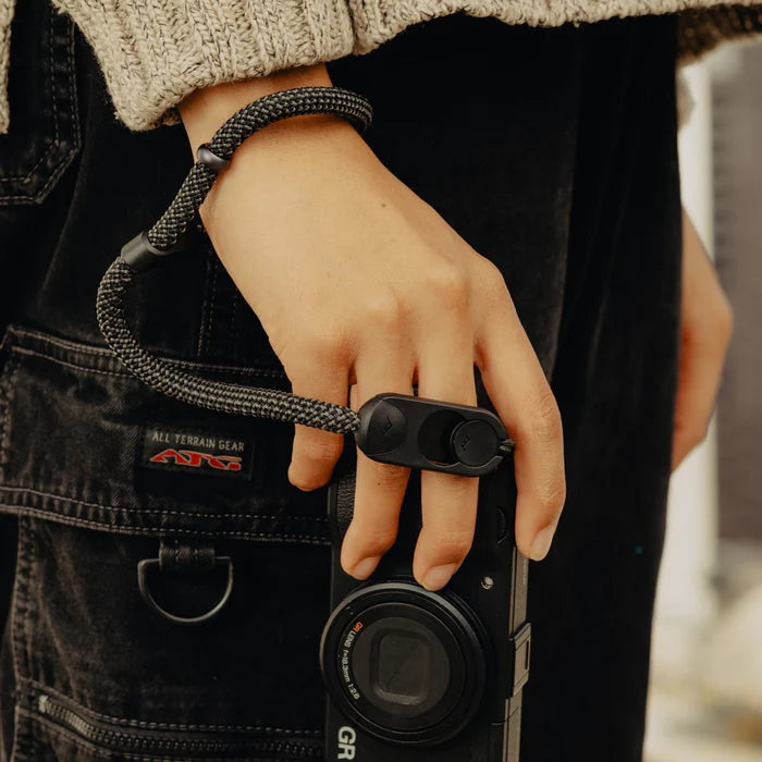Hand holding a camera with a focus on the lens and strap, wearing a bracelet.