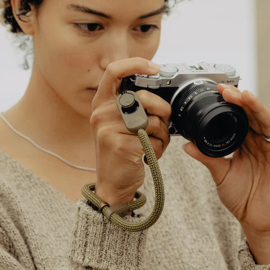 Person holding a camera with a strap, focusing on taking a photo.