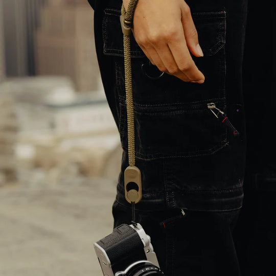 Person holding a camera with a strap, blurred background