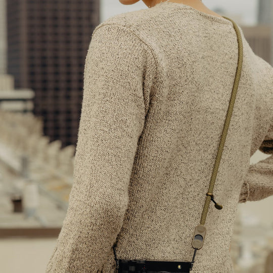 Person wearing a Peak Design Form Rope Camera Strap with a blurred indoor background