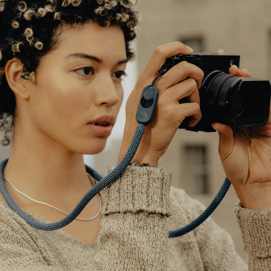 Person holding a camera with a strap, wearing a beige sweater.