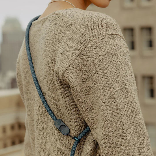 Person wearing a beige sweater with a blue strap over shoulder, blurred cityscape background