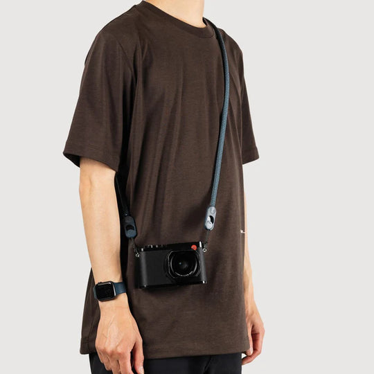 Person wearing a brown t-shirt with a black camera attached to it on a plain background