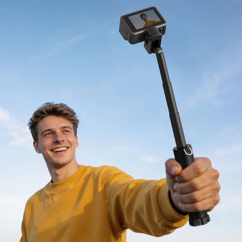Young man smiling and holding an extended Ulanzi MT98 foldable selfie stick mounted with an action camera for vlogging.