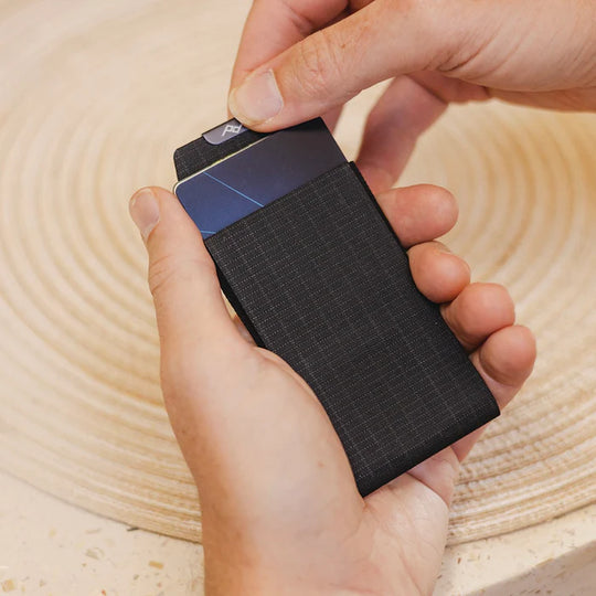 Hand holding a black cardholder with a textured surface on a wooden background